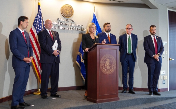 Attorney General Pamela Bondi delivers remarks from a podium at the U.S. Attorney’s Office for the Middle District of Florida. She is joined by federal government officials.